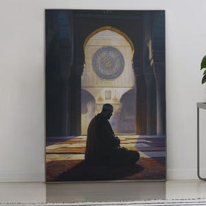 May include: A framed canvas print depicts a person in prayer within an arched structure, bathed in sunlight. The artwork is propped against a white wall, next to two side tables with a plant, books, and a lamp. A striped rug is in the foreground.