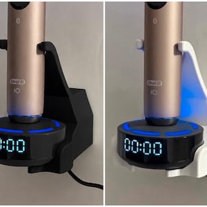 Könnte beinhalten: Zwei Wandhalterungen für Zahnbürsten, eine in Schwarz und eine in Weiß, die jeweils eine roségoldene Oral-B iO elektrische Zahnbürste halten. Die Halterungen haben eine runde Basis mit einer Digitaluhr, die 00:00 anzeigt, und einen blauen Lichtring.