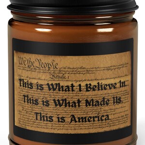 May include: A brown glass candle jar with a black lid and a label that reads "We the People" and "This is What I Believe in. This is What Made Us. This is America."
