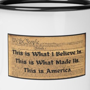 May include: White enamel mug with a black rim. The mug features a vintage-style image of the beginning of the US Constitution with the text "We the People" and the text "This is What I Believe In. This is What Made Us. This is America."