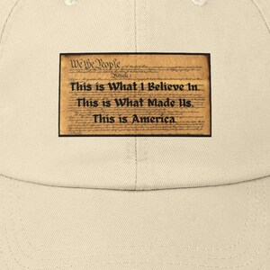 May include: A beige distressed baseball cap with a patch featuring the text "We the People" and "This is What I Believe In... This is What Made Us. This is America."