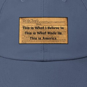 May include: A distressed, dark blue baseball cap with a distressed, faded, brown patch featuring the text "We the People" and "This is What I Believe In... This is What Made Us. This is America."