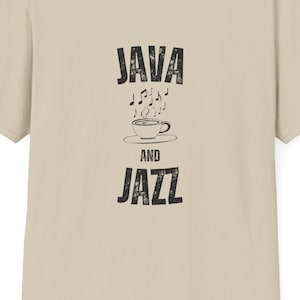 以下が含まれることがあります： ベージュのTシャツに、黒いグラフィックで「JAVA AND JAZZ」と、コーヒーカップと音符が描かれています。
