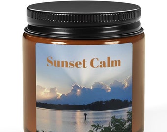 Puede incluir: Un tarro de vela de vidrio marrón con una tapa negra. La etiqueta en el tarro presenta una puesta de sol sobre un lago con el texto "Sunset Calm".