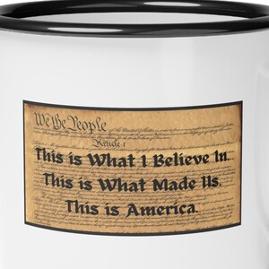 May include: White enamel mug with a black rim and handle. The mug features a printed image of the beginning of the US Constitution with the text "We the People" and the words "This is What I Believe In. This is What Made Us. This is America."