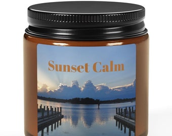 Puede incluir: Un tarro de vidrio marrón para velas con tapa negra. La etiqueta del tarro dice "Sunset Calm" y presenta una fotografía de un lago con un muelle y una puesta de sol.