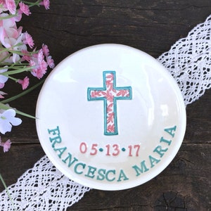 May include: White ceramic dish with a teal cross design filled with pink floral patterns. The dish has the name "FRANCESCA MARIA" and the date "05.13.17" in teal and pink lettering around the edge.