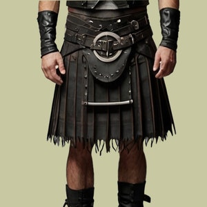 Op de afbeelding: Een zwarte leren kilt met een brede riem en metalen gesp. De kilt heeft een geplooid ontwerp met een gerafelde zoom. De outfit bevat bijpassende leren polsbanden en een decoratief zakje.