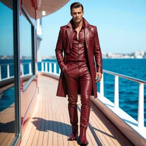 May include: A burgundy leather outfit consisting of a long coat, button-down shirt, and fitted pants. The ensemble is worn with matching burgundy boots. The outfit is worn on a wooden deck with a blue ocean and sky in the background.