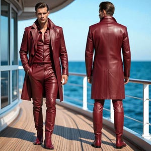 May include: A burgundy leather outfit consisting of a long coat, button-down shirt, pants, and boots. The outfit is worn by a person standing on a wooden deck with a blue ocean in the background. The coat has a classic lapel and a tailored fit.