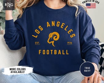 May include: A navy blue sweatshirt with the words "Los Angeles" and "Football" in yellow lettering. The sweatshirt also features a yellow ram head logo and the text "Est. 1936".