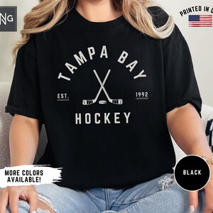 May include: Black t-shirt with a white graphic of crossed hockey sticks and the text "Tampa Bay" with "Est. 1992" and "Hockey" underneath.