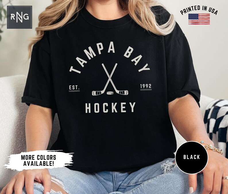 May include: Black t-shirt with a white graphic of crossed hockey sticks and the text "Tampa Bay" with "Est. 1992" and "Hockey" underneath.