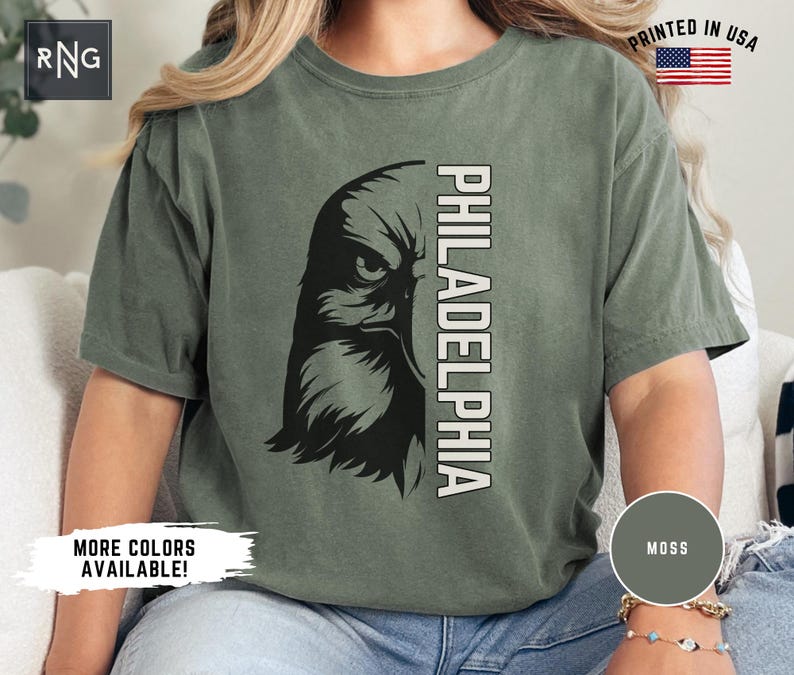 K&ouml;nnte beinhalten: Ein gr&uuml;nes T-Shirt mit einem schwarzen und wei&szlig;en Adler-Motiv und dem Text "PHILADELPHIA" auf der Vorderseite. Das Shirt ist aus einem weichen, bequemen Material gefertigt und hat eine lockere Passform.