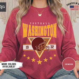May include: A crimson long-sleeve crewneck sweatshirt featuring the yellow text WASHINGTON FOOTBALL above a graphic of a dark red football helmet centred on a yellow triangle. The numbers 19 and 32 flank the helmet, with seven yellow stars below.