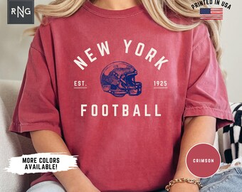 May include: Crimson red t-shirt with a vintage-style graphic of a football helmet and the text "NEW YORK FOOTBALL EST. 1925".
