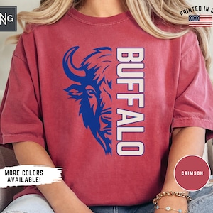 Op de afbeelding: Een roodbruin T-shirt met een blauwe buffelkop-afbeelding en het woord "BUFFALO" in witte tekst. Het shirt is gemaakt van zacht, comfortabel materiaal en heeft een ontspannen pasvorm.