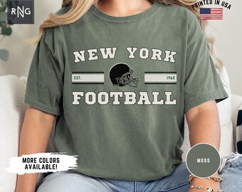 Könnte beinhalten: Ein grünes T-Shirt mit dem Text "NEW YORK FOOTBALL" in Weiß, mit einer schwarzen und weißen Footballhelmgrafik und dem Text "EST. 1960".