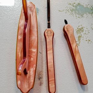 May include: Three vintage, peach-colored, plastic shoe horn tools. The tools have a floral design and are in good condition.