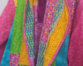 May include: A colorful patchwork jacket with a vibrant mix of patterns and colors. The jacket features a pink exterior, with panels of green, yellow, blue, and purple fabrics. The interior lining is a deep purple. The jacket is hanging on a blue hanger.