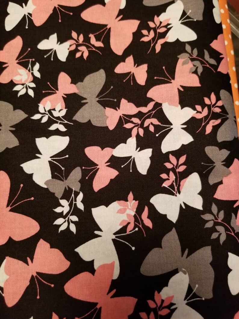 May include: Black fabric with a repeating pattern of pink, white, and gray butterflies. The butterflies are silhouetted against a dark background.
