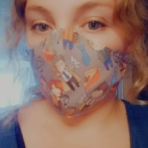 May include: A person wearing a gray face mask with a colorful pattern of cartoon characters and pie slices. The mask has a light gray background with a variety of colors, including blue, red, yellow, and green.