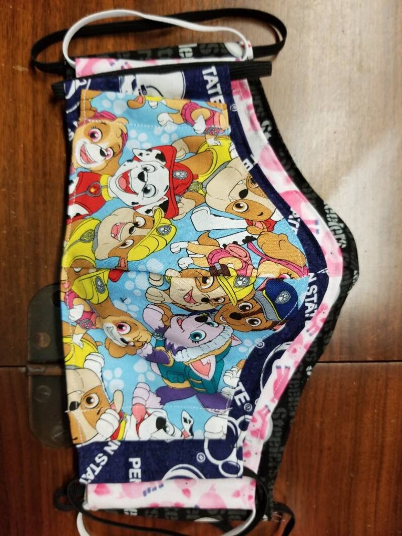 May include: Three layered face masks with a Paw Patrol character print. The outer layer is pink with white polka dots and the text "Paw Star" in black. The middle layer is navy blue with the text "Paw Star" in white. The inner layer is blue with a Paw Patrol character print.