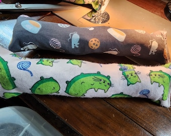 May include: Two catnip toys. One is gray with white and blue designs and the other is white with green cat faces and blue yarn.