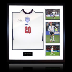 Puede incluir: Camiseta de fútbol inglesa blanca enmarcada con el número 20 en rojo, un logotipo azul de Nike y una firma. Incluye tres fotos de acción de un futbolista. El marco es negro.