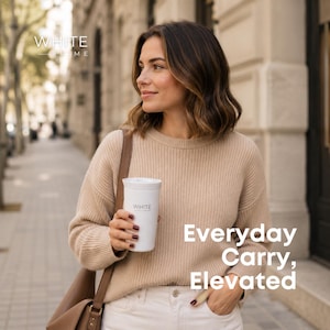 May include: A woman holding a white travel mug with the word "WHITE" printed on it. The mug is cylindrical and has a lid. The text "Everyday Carry, Elevated" is displayed on the right side of the image. The woman is wearing a beige sweater and white pants.