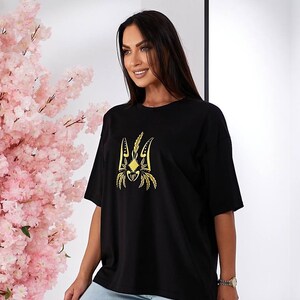 Puede incluir: Camiseta negra de gran tama&ntilde;o con un s&iacute;mbolo de tridente ucraniano bordado en oro.