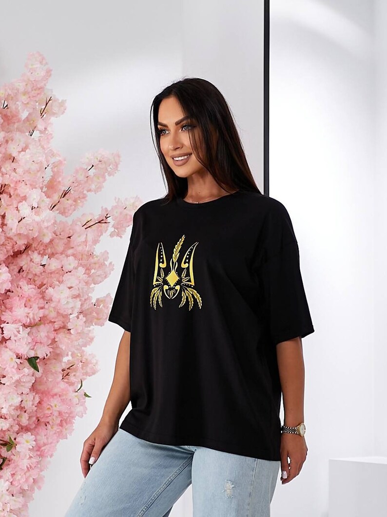 Puede incluir: Camiseta negra de gran tama&ntilde;o con un s&iacute;mbolo de tridente ucraniano bordado en oro.