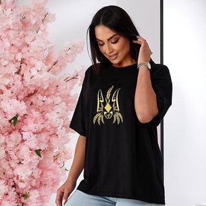Puede incluir: Camiseta negra de gran tama&ntilde;o con un s&iacute;mbolo de tridente ucraniano bordado en oro.