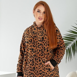 Pode incluir: Um moletom marrom e preto com estampa de leopardo, bolso canguru e capuz com cordão.