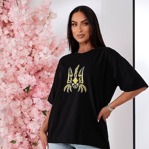 Puede incluir: Camiseta negra de gran tama&ntilde;o con un s&iacute;mbolo de tridente ucraniano bordado en oro.