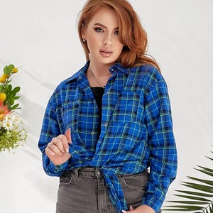 Pode incluir: Uma camisa de flanela xadrez azul e verde com mangas compridas e fecho de botões. A camisa está amarrada na cintura.