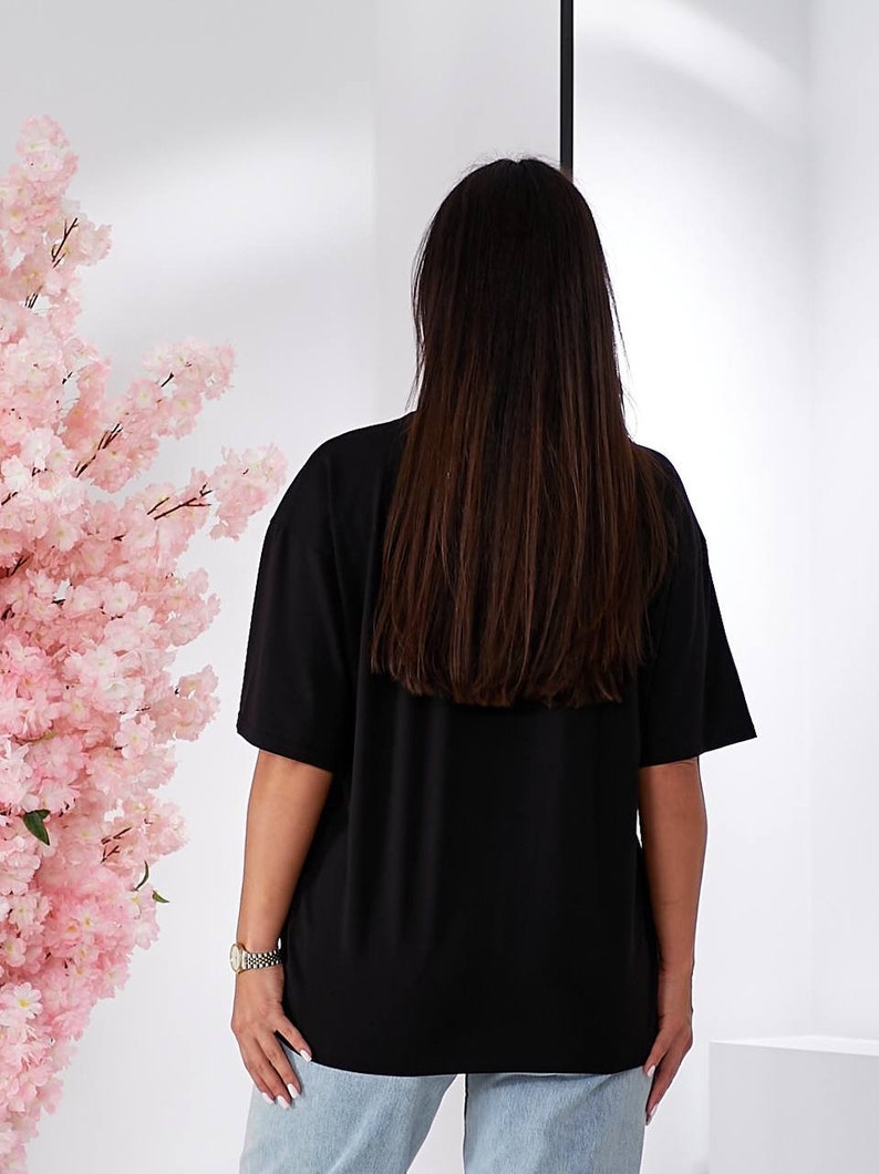 Puede incluir: Una camiseta negra de gran tama&ntilde;o con mangas cortas. La camiseta la lleva puesta una persona que lleva unos vaqueros azules claros.