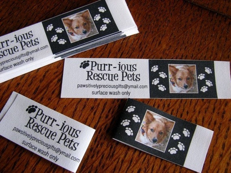 K&ouml;nnte beinhalten: Ein wei&szlig;er rechteckiger Aufkleber mit schwarzem Text, der "Purr-ious Rescue Pets" und die E-Mail-Adresse "pawsitivelypreciousgifts@ymail.com" lautet. Der Text "surface wash only" ist ebenfalls enthalten. Der Aufkleber hat einen schwarzen Rand und Pfotenabdr&uuml;cke an den R&auml;ndern. Ein Foto eines Hundes befindet sich in der Mitte des Aufklebers.