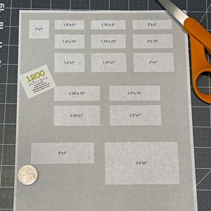 Pu&ograve; includere: Un foglio di carta bianco con una griglia di rettangoli etichettati con diverse misure in pollici. Il foglio &egrave; su una superficie di griglia nera. Il testo "1200 stitches" &egrave; visibile nell'angolo in basso a sinistra.