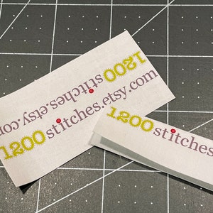 K&ouml;nnte beinhalten: Zwei wei&szlig;e Etiketten mit gelbem Text und roten Punkten. Der Text auf den Etiketten lautet "1200 stitches.etsy.com".