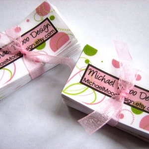 Pu&ograve; includere: Un mazzo di biglietti da visita bianchi con un design astratto rosa e verde. I biglietti presentano il testo "Moo Design" e "sign.etsy.com". I biglietti sono legati insieme da un nastro rosa.