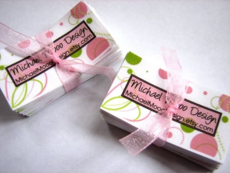Pu&ograve; includere: Un mazzo di biglietti da visita bianchi con un design astratto rosa e verde. I biglietti presentano il testo "Moo Design" e "sign.etsy.com". I biglietti sono legati insieme da un nastro rosa.