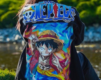 May include: Black denim jacket featuring a colourful graphic of a character from the anime series One Piece. The back of the jacket displays the show's logo in blue and white.