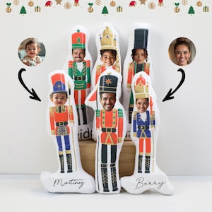 May include: Seven personalized nutcracker ornaments with different faces and names. The ornaments are made of fabric and have a white background with colorful details. The names on the ornaments are "Martinez" and "Berry".