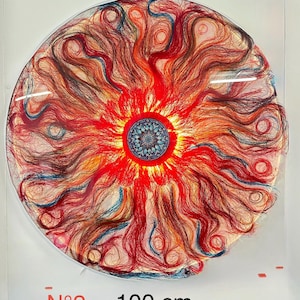 Op de afbeelding: Een rond kunstwerk met een zonachtig ontwerp. Het stuk heeft een centraal blauw mandala, omgeven door stralende rode en oranje strengen, met vleugjes blauw. Het kunstwerk heeft een diameter van 100 cm.