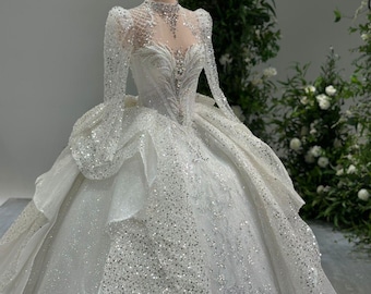 May include: A white wedding dress with a long, flowing skirt and a fitted bodice. The dress is covered in sparkling sequins and has a high neckline. The dress is being displayed on a mannequin.