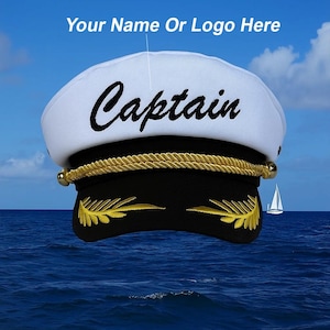 May include: A white captain's hat with the word "Captain" in black script. The hat has a gold rope trim and gold leaf accents on the black visor. The text "Your Name Or Logo Here" is above the hat. The background is a blue sky and ocean.