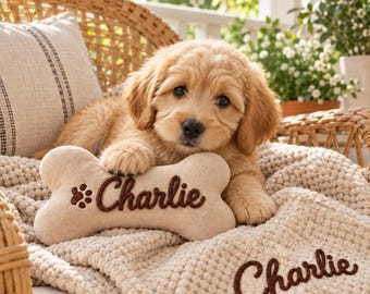 May include: A light beige, textured, bone-shaped plush toy with the name Charlie and a paw print embroidered in dark brown thread, resting next to a matching beige textured blanket featuring the name Charlie embroidered in dark brown thread.