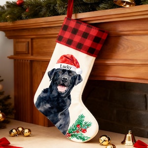 May include: Christmas stocking with a black Labrador Retriever wearing a Santa hat with the name "Lucky". The stocking has a red and black buffalo plaid cuff and is decorated with a sprig of greenery and red berries.
