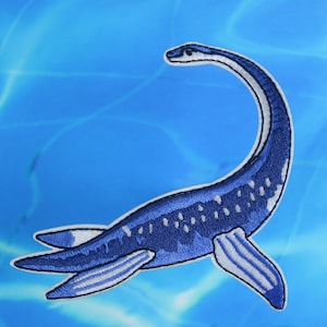 Könnte beinhalten: Ein blauer gestickter Aufnäher mit einem Plesiosaurus, der im Meer schwimmt. Der Plesiosaurus hat einen langen Hals und Flossen.